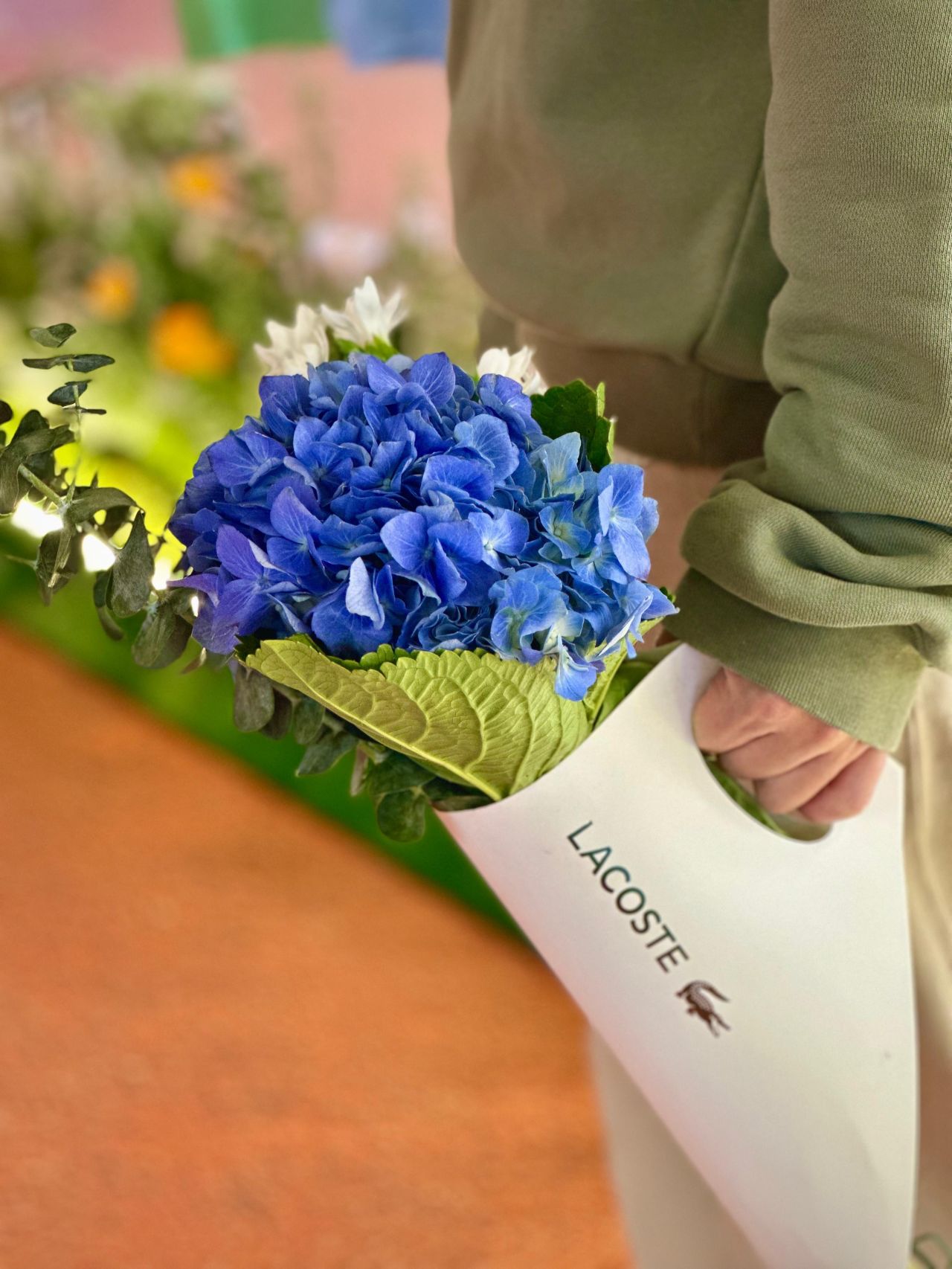 A visitor holding a blue hydrangea bouquet in Lacoste wrapping